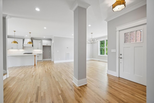 entryway featuring decorative columns, crown molding, and light wood-type flooring