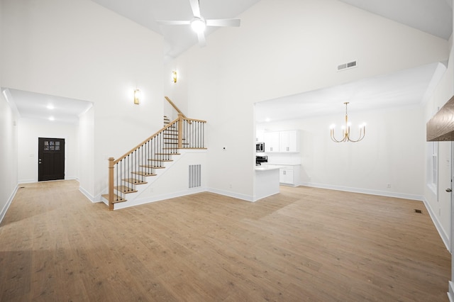 unfurnished living room featuring ceiling fan with notable chandelier, high vaulted ceiling, and light wood-type flooring