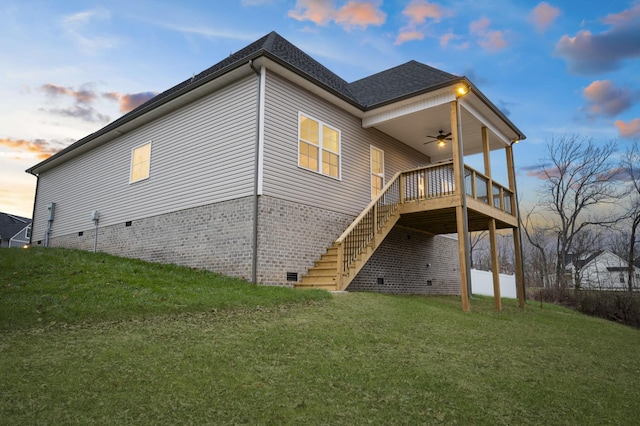 back house at dusk featuring a wooden deck, a lawn, and ceiling fan