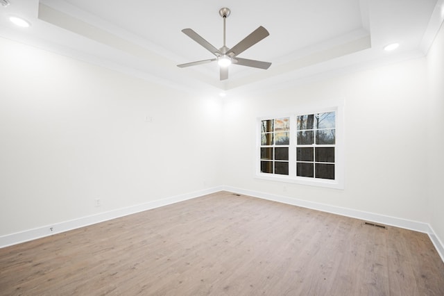 empty room featuring ceiling fan, ornamental molding, wood-type flooring, and a raised ceiling