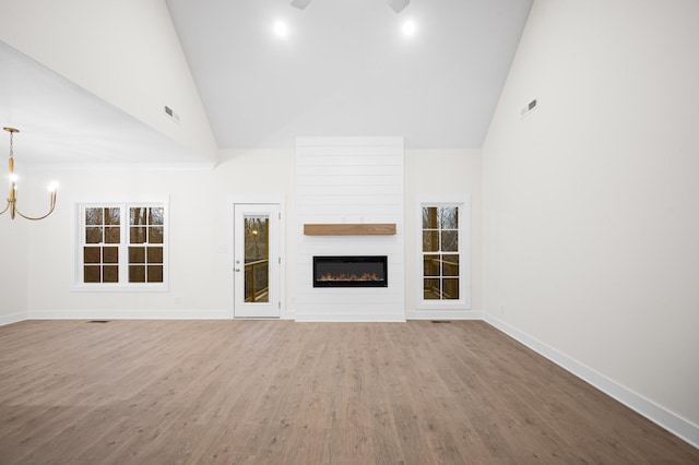 unfurnished living room with hardwood / wood-style flooring, a large fireplace, ceiling fan with notable chandelier, and high vaulted ceiling