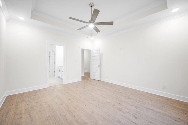 unfurnished bedroom featuring crown molding, a tray ceiling, light hardwood / wood-style floors, and ensuite bathroom