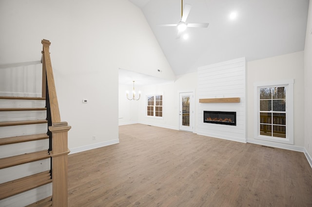 unfurnished living room with hardwood / wood-style flooring, a large fireplace, ceiling fan with notable chandelier, and high vaulted ceiling