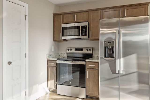 kitchen with light stone counters, stainless steel appliances, and light wood-type flooring