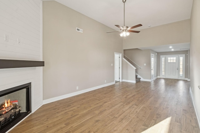 unfurnished living room with ceiling fan, a large fireplace, high vaulted ceiling, and light hardwood / wood-style flooring