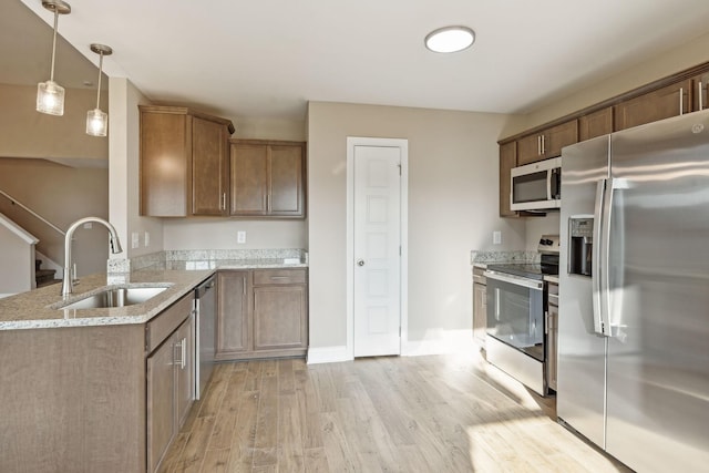 kitchen with sink, stainless steel appliances, light stone countertops, decorative light fixtures, and light wood-type flooring