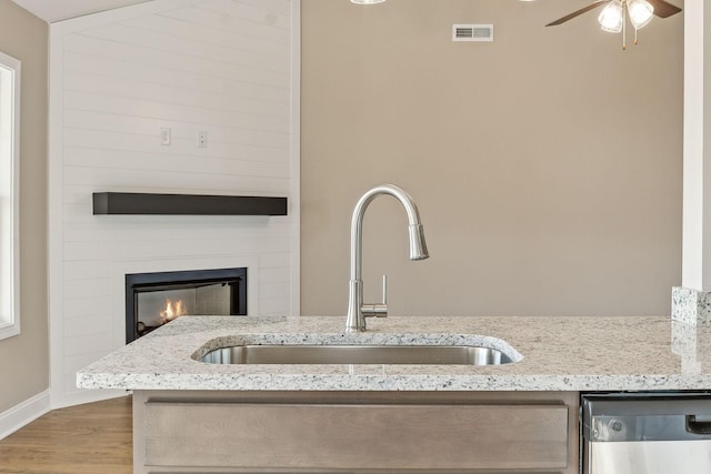 room details with sink, stainless steel dishwasher, a large fireplace, ceiling fan, and hardwood / wood-style floors