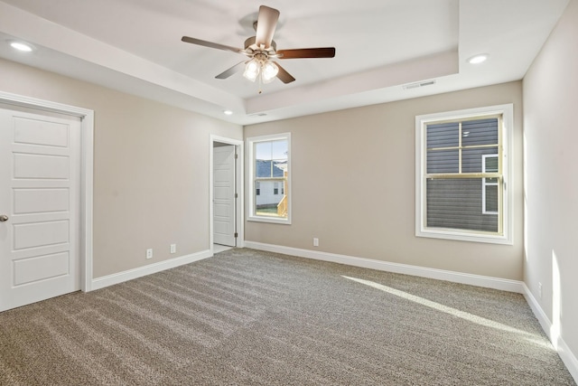 carpeted spare room with a tray ceiling and ceiling fan