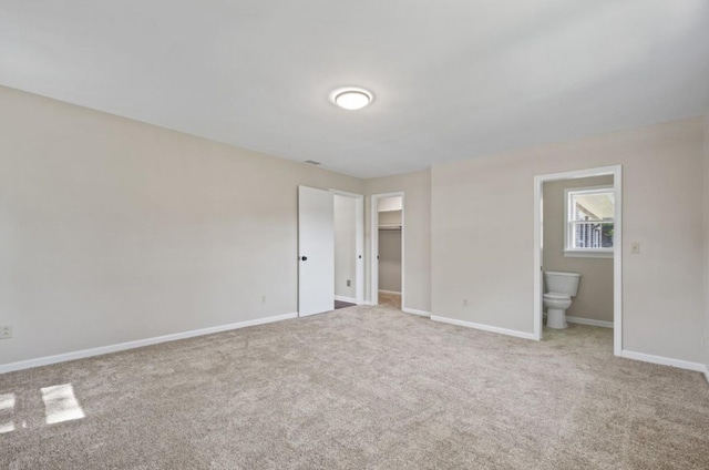 unfurnished bedroom featuring a walk in closet, light colored carpet, a closet, and ensuite bathroom