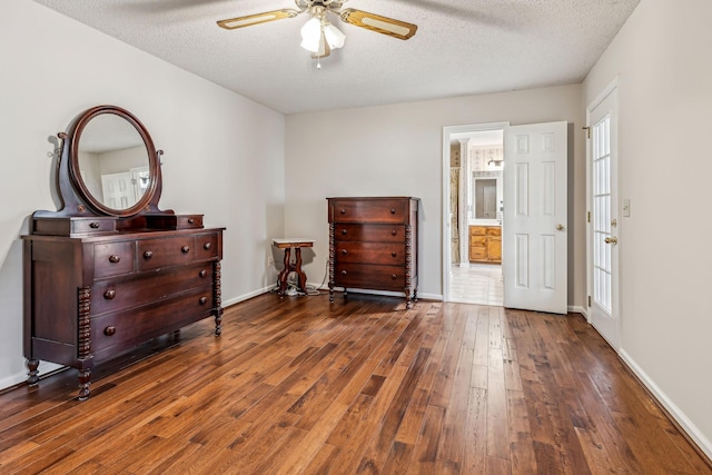 bedroom featuring ceiling fan, ensuite bath, dark hardwood / wood-style flooring, and a textured ceiling