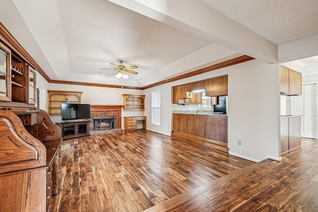 unfurnished living room with dark wood-type flooring, a brick fireplace, a textured ceiling, a tray ceiling, and ceiling fan