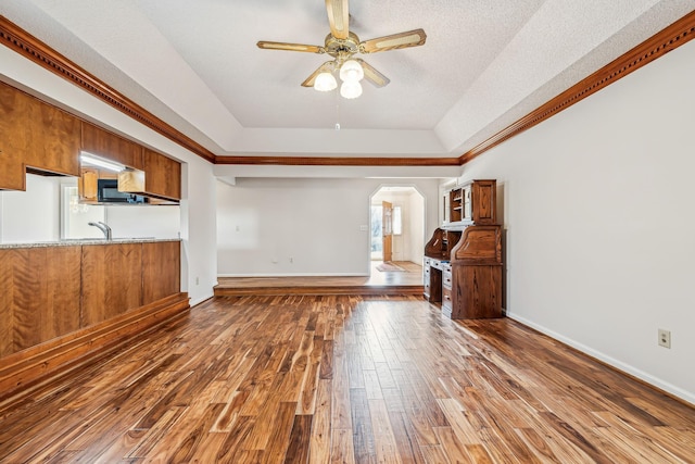 unfurnished living room featuring sink, ceiling fan, hardwood / wood-style floors, a textured ceiling, and a raised ceiling