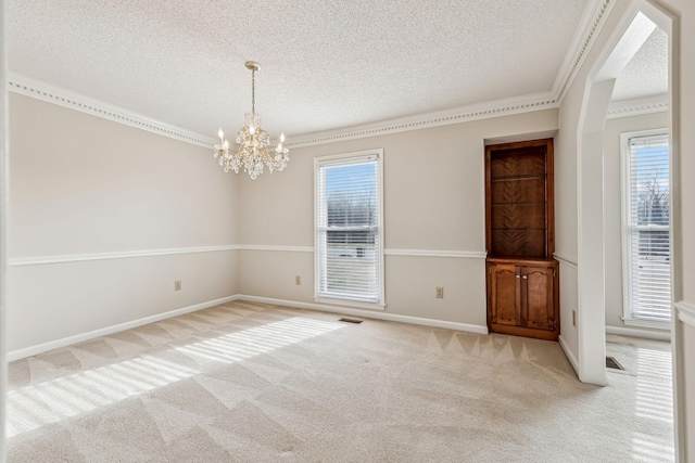 carpeted empty room featuring crown molding, a wealth of natural light, a textured ceiling, and a chandelier