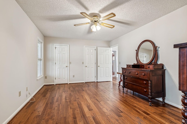 bedroom with multiple closets, ceiling fan, dark wood-type flooring, and a textured ceiling