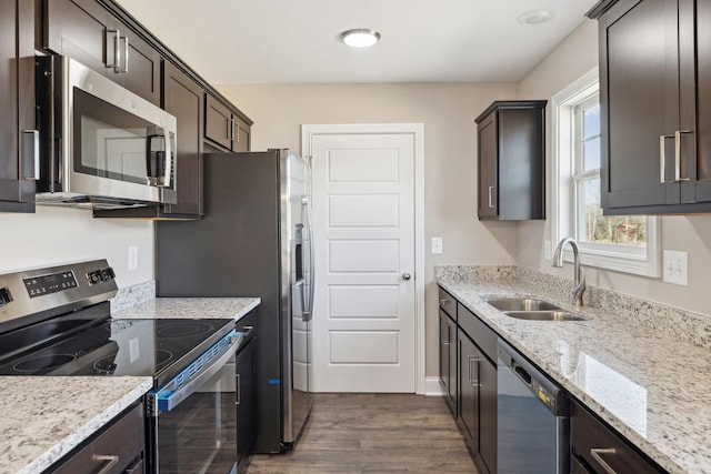 kitchen with sink, dark wood-type flooring, stainless steel appliances, light stone countertops, and dark brown cabinets