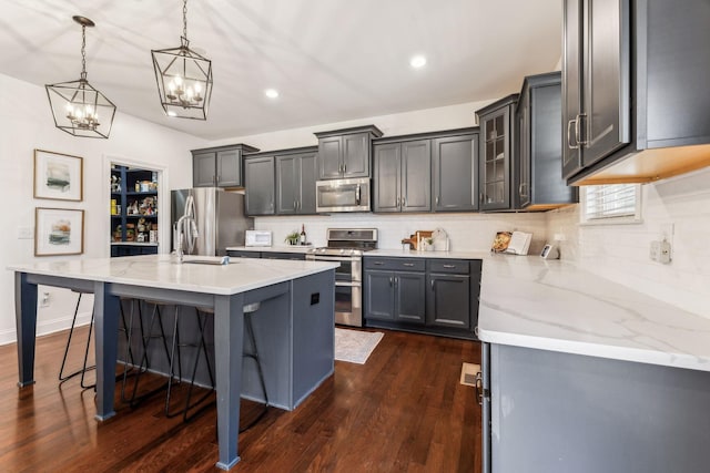 kitchen with decorative light fixtures, sink, a kitchen bar, stainless steel appliances, and a center island with sink