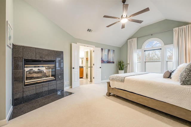 carpeted bedroom featuring a tiled fireplace, lofted ceiling, ceiling fan, and ensuite bath