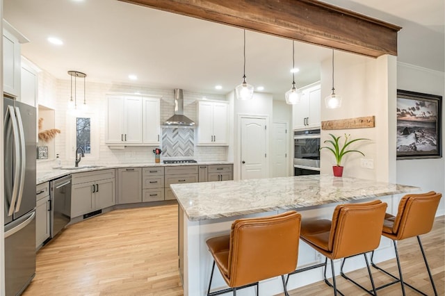 kitchen featuring white cabinetry, sink, hanging light fixtures, stainless steel appliances, and wall chimney range hood