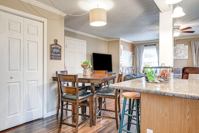 dining space with dark wood-type flooring, ornamental molding, and a textured ceiling