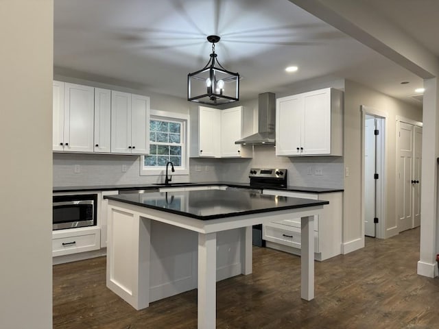 kitchen featuring decorative light fixtures, white cabinets, a center island, stainless steel appliances, and wall chimney exhaust hood