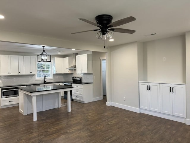 kitchen with wall chimney range hood, appliances with stainless steel finishes, white cabinetry, hanging light fixtures, and a kitchen island