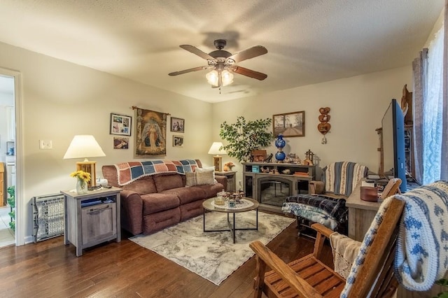 living room featuring dark wood-type flooring, ceiling fan, and a textured ceiling