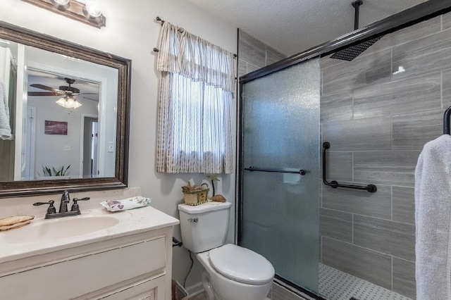 bathroom featuring vanity, walk in shower, ceiling fan, toilet, and a textured ceiling