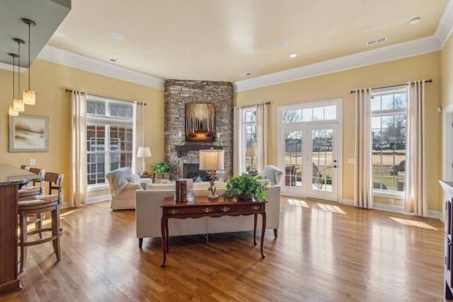 living room with crown molding, a stone fireplace, and wood-type flooring