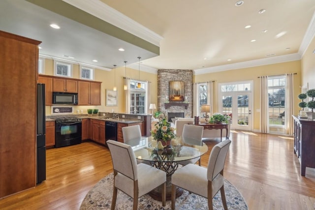 dining area with ornamental molding, a stone fireplace, sink, and light wood-type flooring