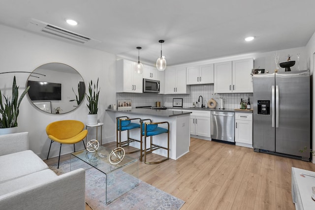 kitchen with decorative light fixtures, white cabinetry, a kitchen bar, decorative backsplash, and stainless steel appliances