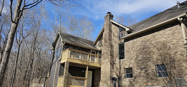 exterior space with brick siding, a chimney, and a balcony