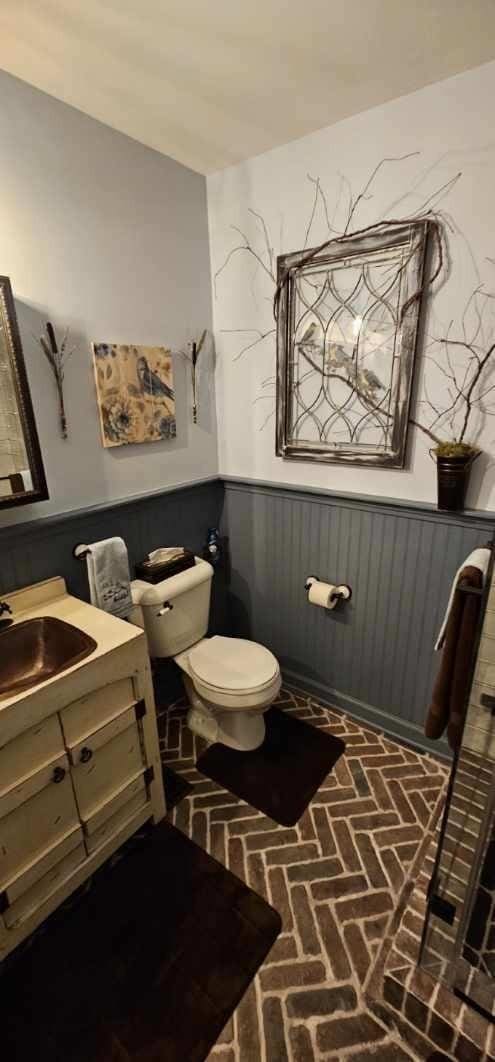 bathroom featuring toilet, brick floor, vanity, and wainscoting