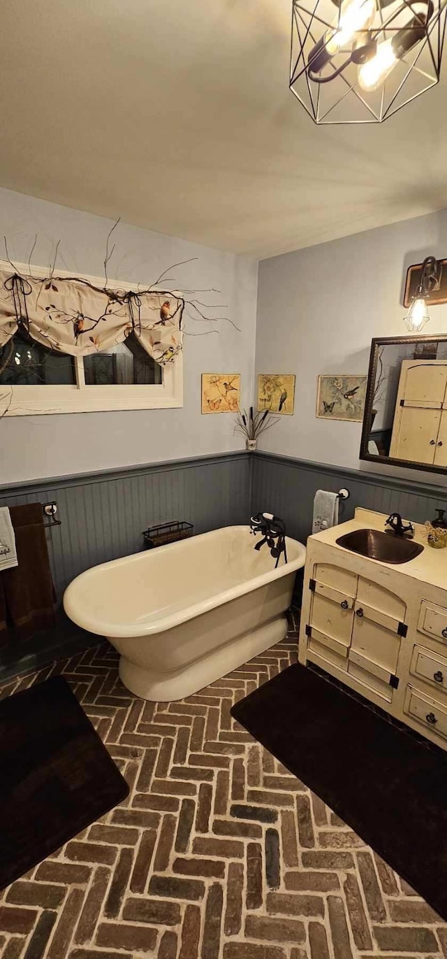 bathroom featuring brick floor, wainscoting, a freestanding bath, and vanity