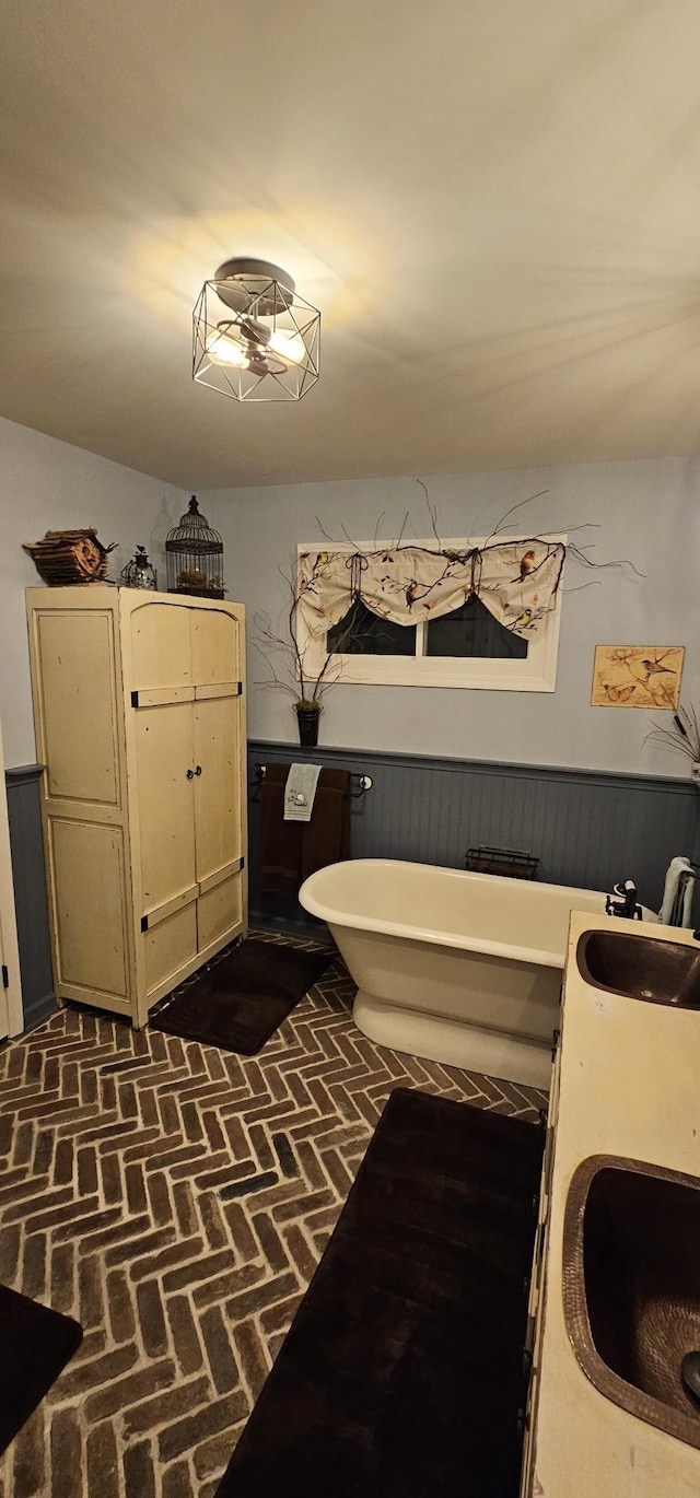 bathroom featuring a sink, wainscoting, brick floor, and a freestanding tub