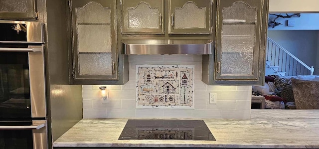 kitchen featuring range hood, black electric stovetop, backsplash, glass insert cabinets, and oven