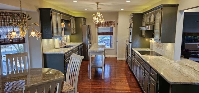 kitchen featuring dark wood-type flooring, a sink, appliances with stainless steel finishes, backsplash, and an inviting chandelier