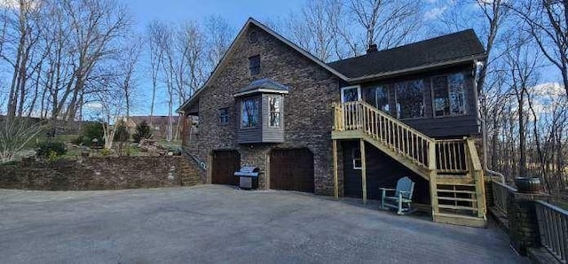 exterior space featuring a garage, driveway, stone siding, a chimney, and stairs