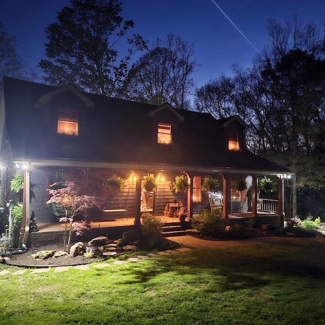back of house at night featuring a porch and a lawn
