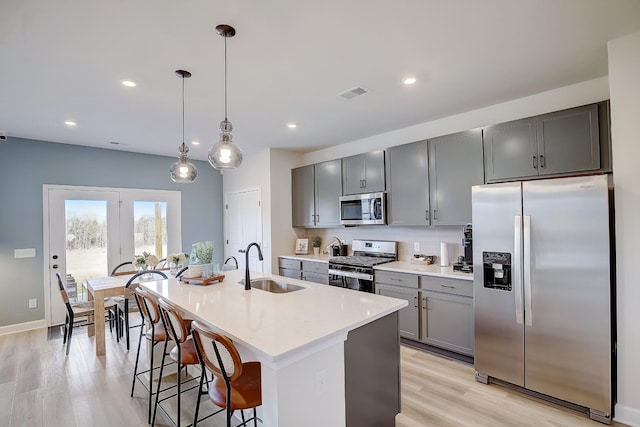 kitchen featuring a breakfast bar, sink, a center island with sink, appliances with stainless steel finishes, and pendant lighting