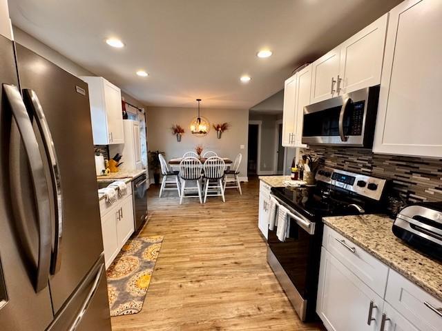 kitchen featuring white cabinetry, light hardwood / wood-style flooring, pendant lighting, stainless steel appliances, and backsplash