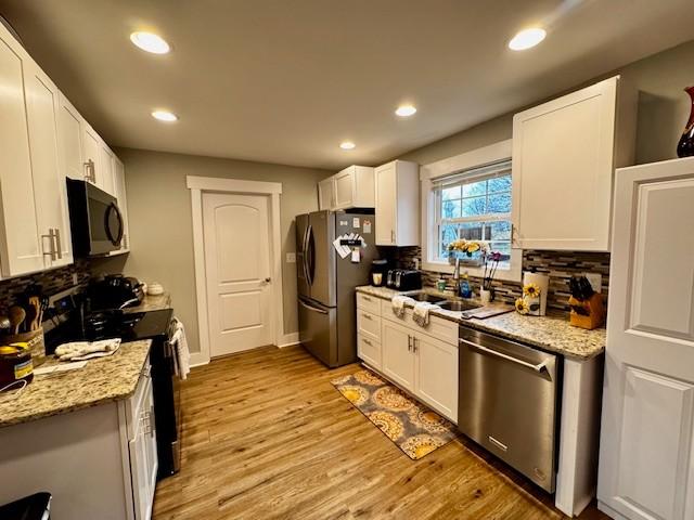 kitchen with white cabinetry, sink, light stone countertops, and appliances with stainless steel finishes