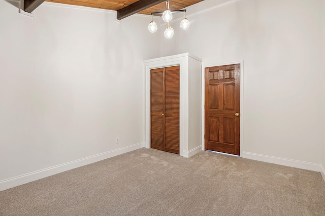 unfurnished bedroom featuring light carpet, beam ceiling, wooden ceiling, and a closet