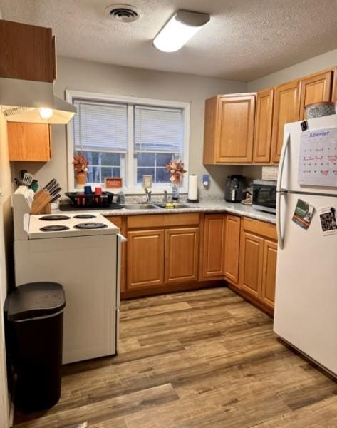 kitchen with white appliances, exhaust hood, a textured ceiling, and light wood-type flooring