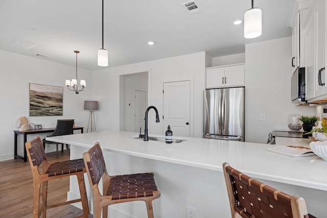 kitchen with pendant lighting, sink, stainless steel refrigerator, white cabinetry, and light hardwood / wood-style floors