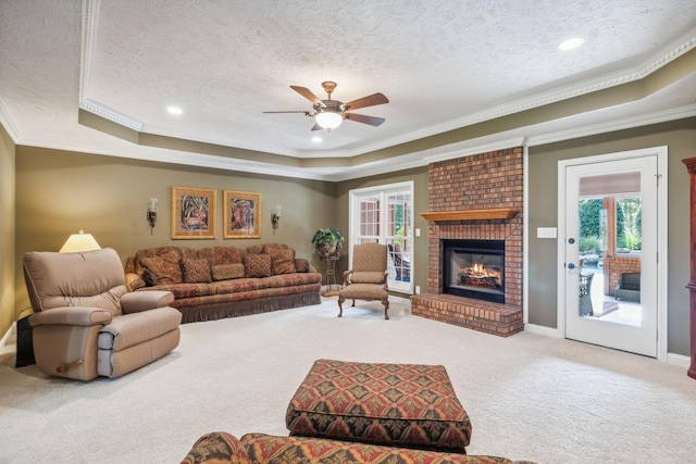 carpeted living room featuring a raised ceiling, crown molding, a brick fireplace, and a textured ceiling