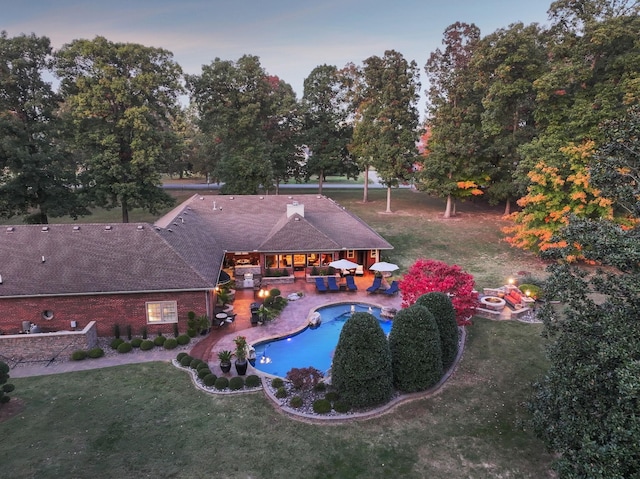 pool at dusk featuring a fire pit, a lawn, and a patio