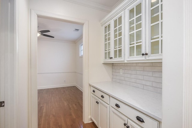 bar with white cabinetry, backsplash, dark hardwood / wood-style flooring, ceiling fan, and crown molding