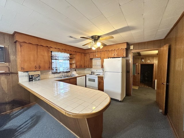 kitchen with sink, white appliances, wooden walls, tile counters, and kitchen peninsula