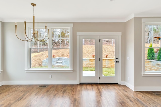 doorway with wood-type flooring, a notable chandelier, and crown molding