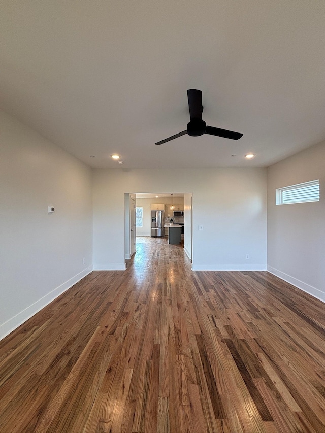 unfurnished living room featuring dark wood-type flooring and ceiling fan